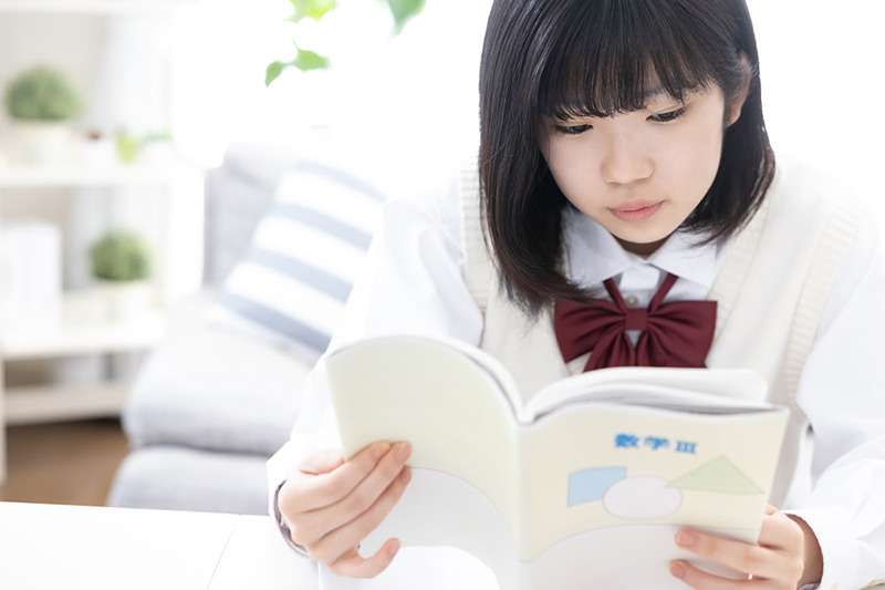 数学の教科書を読んでいる白いベストを着た女子生徒